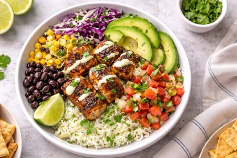Blackened fish taco bowl with cilantro-lime rice, cabbage slaw, avocado, pico de gallo, beans, corn, and creamy lime drizzle.