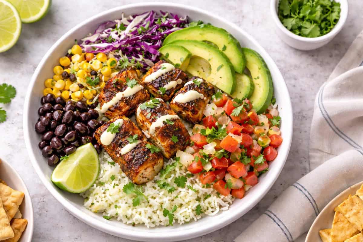 Blackened fish taco bowl with cilantro-lime rice, cabbage slaw, avocado, pico de gallo, beans, corn, and creamy lime drizzle.