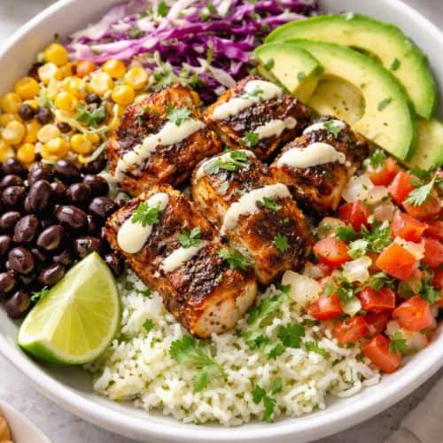 Blackened fish taco bowl with cilantro-lime rice, cabbage slaw, avocado, pico de gallo, beans, corn, and creamy lime drizzle.