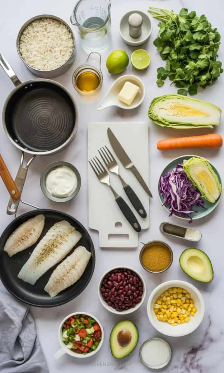 Ingredients and tools for blackened fish taco bowls arranged on white marble, including fish, rice, cabbage, beans, corn, pico, avocado, and sauce ingredients.