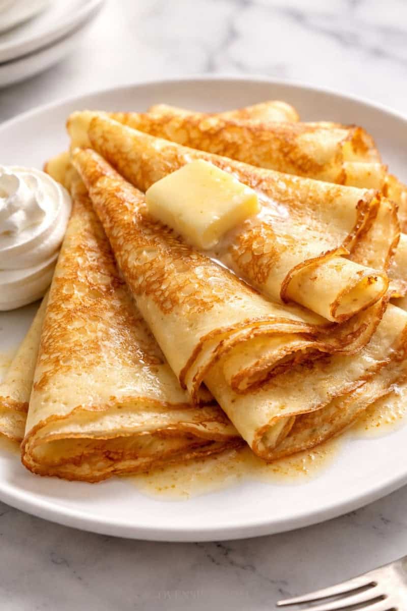 Carnivore cream cheese crepes stacked on a white plate with butter melting on top.