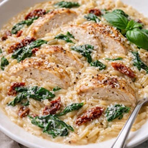Creamy one pot chicken orzo on a white plate with spinach, parmesan, and parsley.