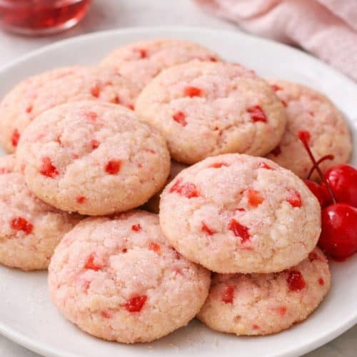 Soft maraschino cherry sugar cookies with chopped cherry pieces served on a white plate.