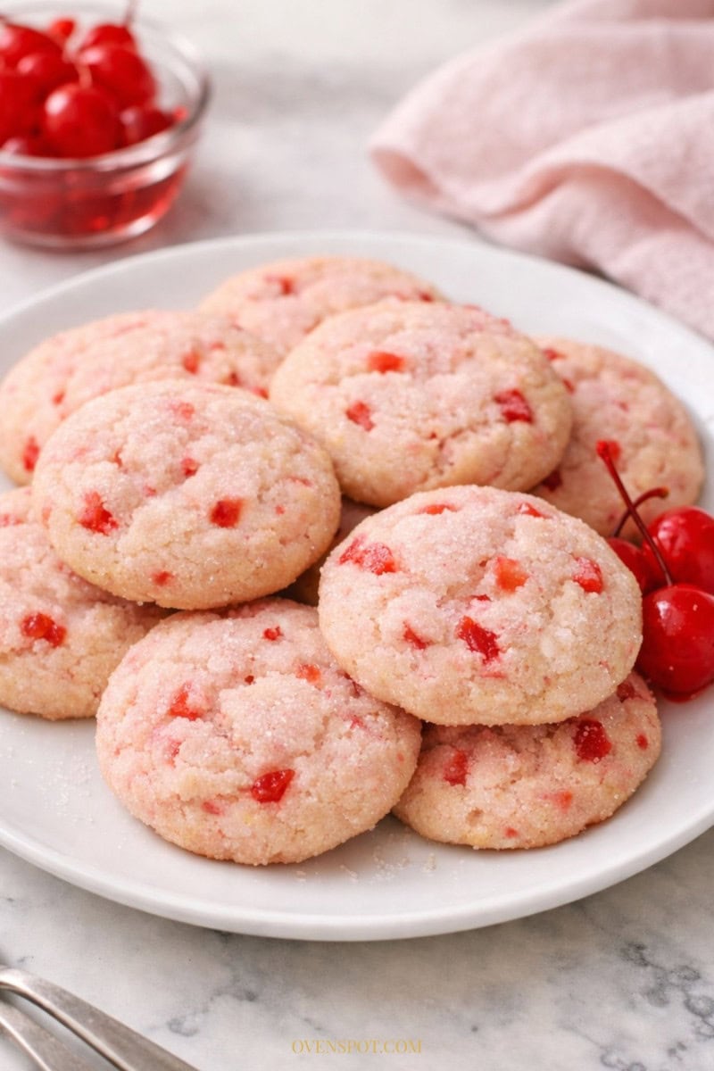 Soft maraschino cherry sugar cookies with chopped cherry pieces served on a white plate.