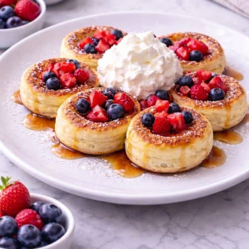 Mini German pancakes with powdered sugar, berries, maple syrup and cream.
