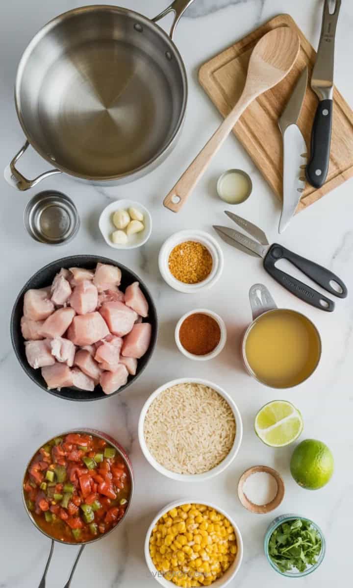 Ingredients and tools for one pot chicken taco skillet arranged on white marble, including chicken, rice, beans, cheese, and a skillet.