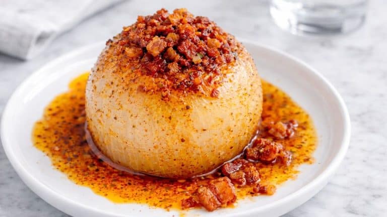 Whole onion boil on a small white plate with buttery spice sauce and crispy bacon
