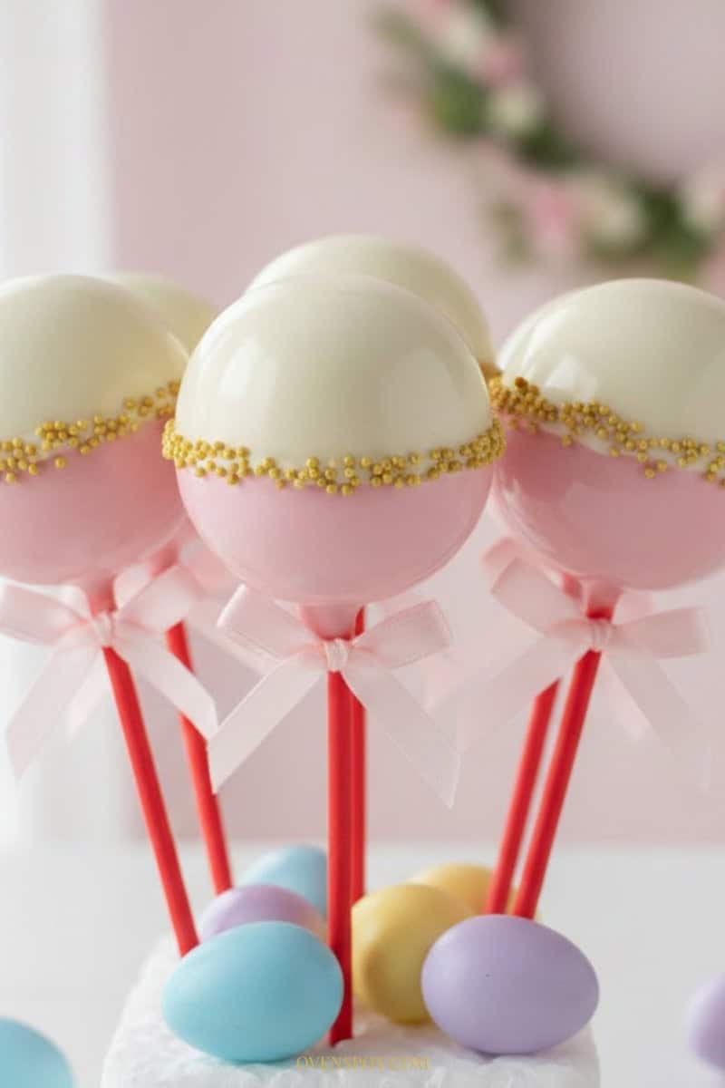 Red velvet Easter cake pops coated in white chocolate with red sprinkles, displayed upright in a glass jar filled with rice
