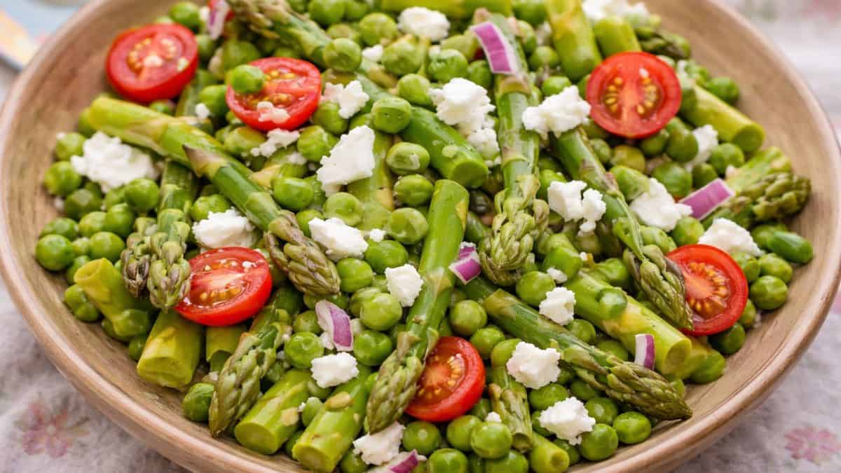 Close-up of asparagus and pea salad with cherry tomatoes, red onion, and crumbled feta cheese