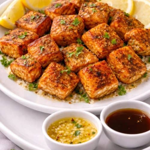 Crispy air fryer salmon bites on a white plate with parsley, lemon, and dipping sauce.