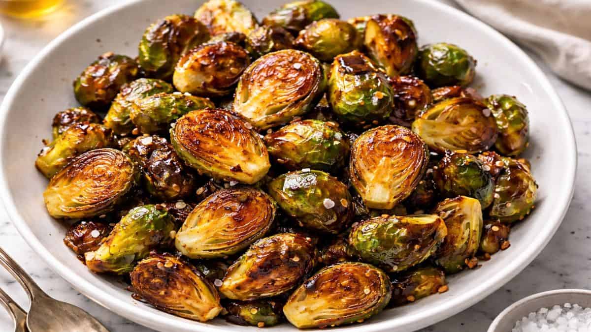 Honey garlic roasted Brussels sprouts in a white bowl, sticky honey garlic glaze shining on crispy roasted sprouts with a sprinkle of sea salt and chili flakes