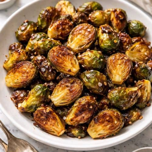 Honey garlic roasted Brussels sprouts with caramelized edges and a glossy glaze on a white plate, sprinkled with flaky sea salt