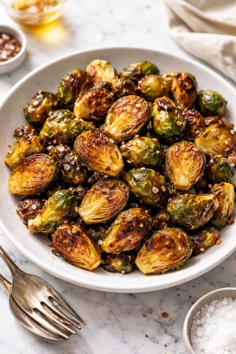 Honey garlic roasted Brussels sprouts with caramelized edges and a glossy glaze on a white plate, sprinkled with flaky sea salt