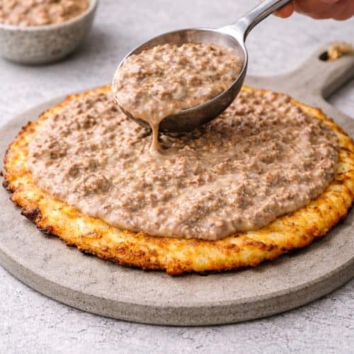 carnivore meat pizza sauce being spooned onto a chicken pizza base