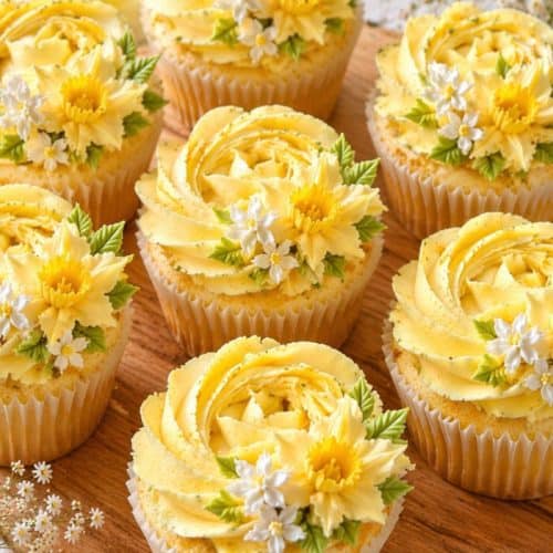 Fresh yellow spring floral cupcakes decorated with delicate floral piping on a wooden board