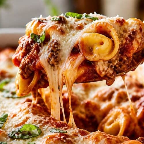Cheesy beef tortellini bake with marinara and melted mozzarella on a white plate.