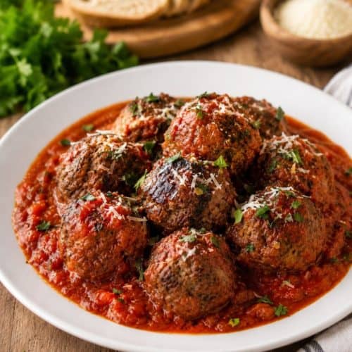 Italian meatballs Copycat Bobby Flay recipe in tomato sauce on a white plate with fresh basil and Parmesan.