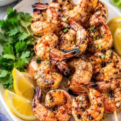 grilled shrimp skewers served with lemon wedges and corriander