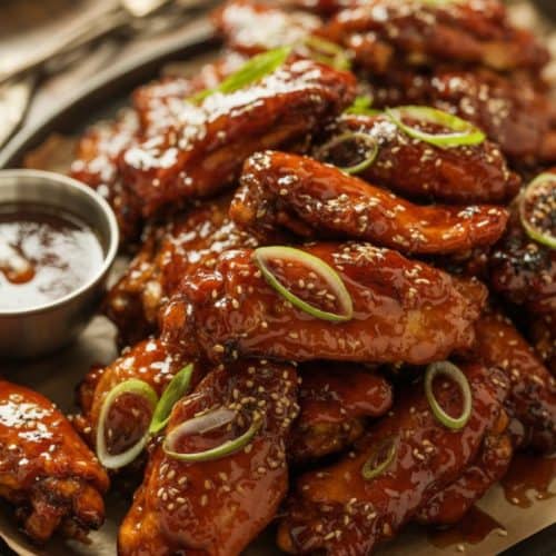 Crispy honey garlic chicken wings coated in a sticky caramelized glaze, topped with sesame seeds and spring onions, served on a rustic platter.