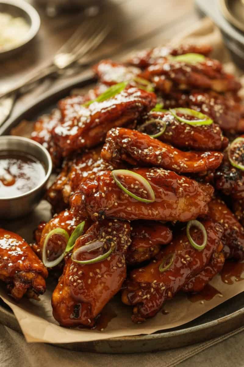 Crispy honey garlic chicken wings coated in a sticky caramelized glaze, topped with sesame seeds and spring onions, served on a rustic platter.