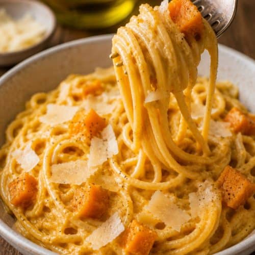 creamy butternut squash pasta with roasted squash pieces and shaved Parmesan, with a fork lifting a twirl of pasta from the bowl