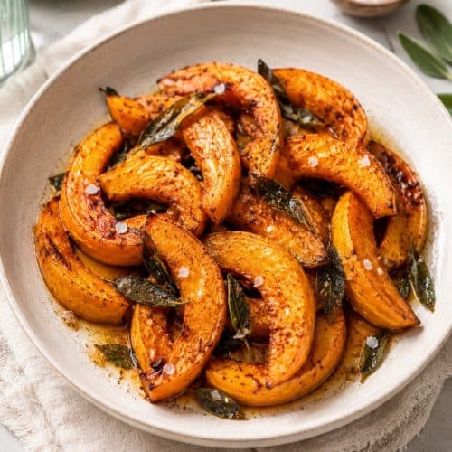roasted pumpkin wedges with caramelized edges, brown butter, crispy sage leaves, black pepper, and flaky salt served in a rustic ceramic bowl